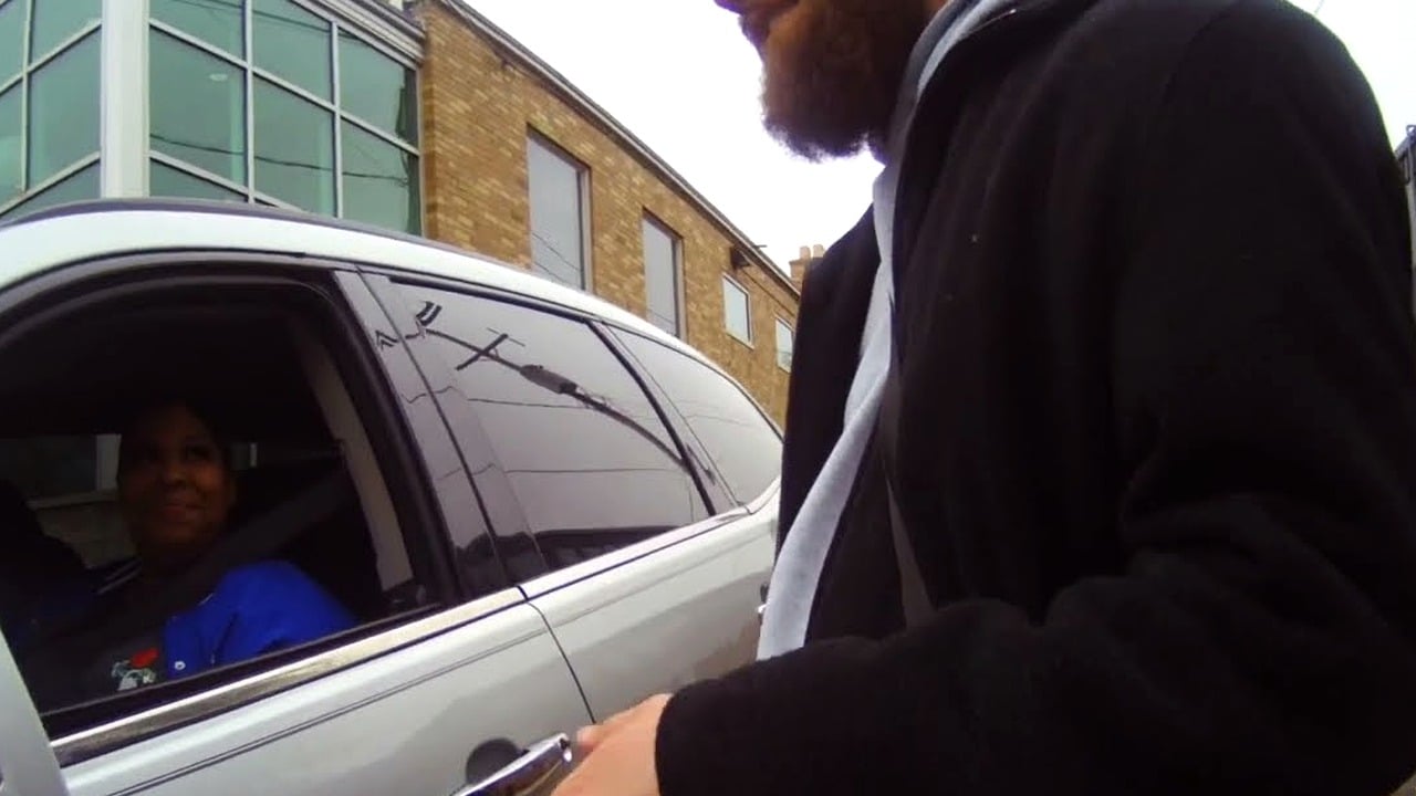 A man speaking with a woman seated in a vehicle.